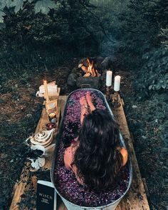 a woman sitting in a bathtub next to a campfire with candles on it