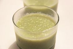 two glasses filled with green liquid sitting on top of a white table next to each other