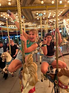 two girls riding on a merry go round at an amusement park with other people in the background