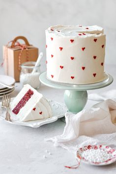 a white cake with red hearts on it sitting on a table next to other plates