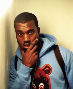 a man in a blue hoodie is holding his hand to his face and looking at the camera