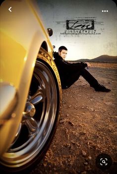 a man sitting on the ground next to a yellow car