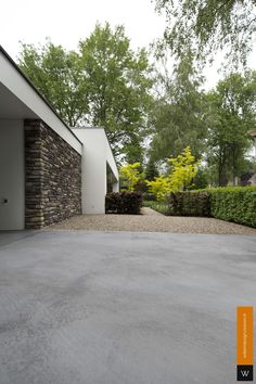 an empty driveway in front of a house with trees and bushes around the entrance area