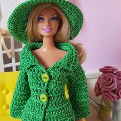 a doll wearing a green jacket and hat with buttons on the front, standing next to a yellow chair