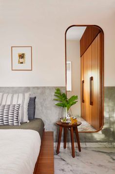 a bedroom with a bed, mirror and plant on the table in front of it