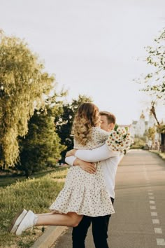 two people walking down the street with their arms around each other and one person holding flowers