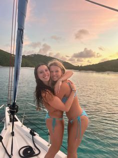 two women in bikinis are hugging on a boat