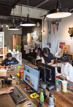 several people working on computers in an office setting with hanging lights above the desks