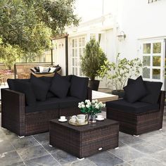 an outdoor living room with wicker furniture and black cushions