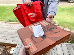 a person holding a large red bag in front of a cardboard box with the letter f on it