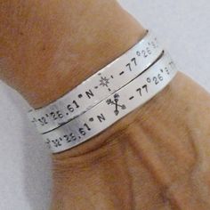 a person's wrist with two silver bracelets on top of it and numbers