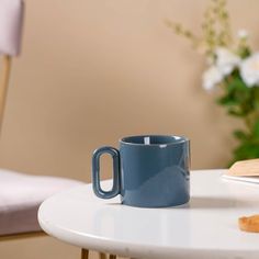 a blue coffee mug sitting on top of a white table next to a wooden spoon