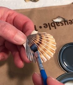 a person holding a paint brush and some seashells in front of a cardboard box