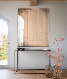 a mirror and vase on a table in front of a door with an arched window