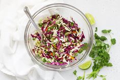 a glass bowl filled with coleslaw and garnished with lime wedges