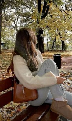 a woman sitting on top of a wooden bench in the park with her handbag