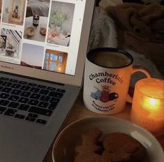 a laptop computer sitting on top of a desk next to a plate of cookies and a cup of coffee