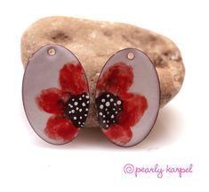 a pair of red and black flower shaped earrings on top of a piece of rock