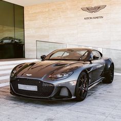 a grey sports car parked in front of a building with the name aston martin on it