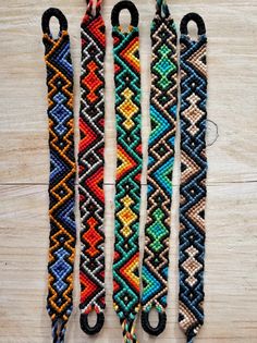 four bracelets with different colors and designs hanging on a wooden table next to each other