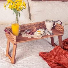 a breakfast tray on a bed next to a vase with yellow flowers and an orange juice