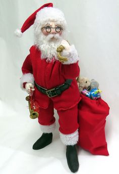 a santa clause doll is holding a teddy bear in his hand and standing next to a red bag