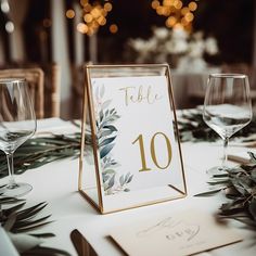 a table set up with place cards, wine glasses and greenery on the table