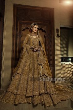 a woman in a golden wedding gown standing on steps with her hands behind her head