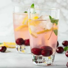 two glasses filled with cherries and lemonade next to cranberries on a table