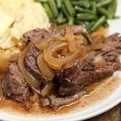 a white plate topped with meat, onions and green beans next to mashed potatoes