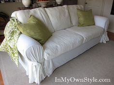 a white couch sitting on top of a hard wood floor covered in green and white pillows