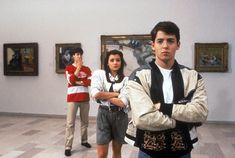 three people are standing in an art museum with paintings on the wall and one person is holding his arms crossed