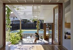 a woman sitting at a table in front of an open air swimming pool with wooden flooring