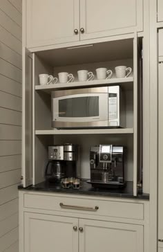 a coffee maker and some cups in a cabinet with white cupboards on the wall