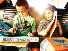 two young boys sitting in the back of a car with their skateboards on display