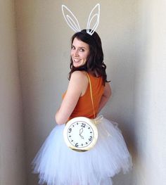 a woman in bunny ears holding a clock and wearing a tutu skirt while standing next to a wall