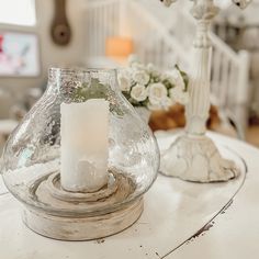 a candle is sitting in a glass vase on a table with white flowers and candlesticks