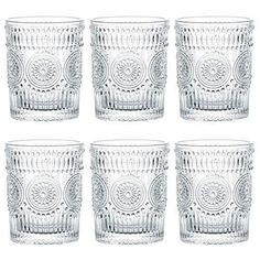 six clear glass tumblers are lined up on a white surface with an intricate design in the middle