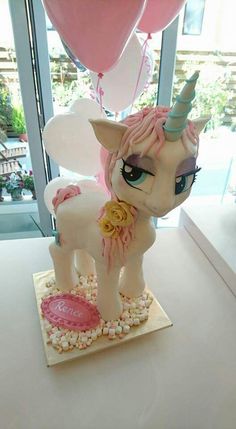 there is a cake that looks like a pony with balloons in the air behind it