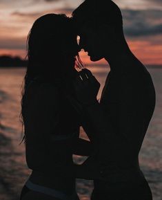 two people standing next to each other in front of the ocean at sunset or sunrise