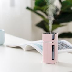 a pink electronic device sitting on top of a white table next to a cup and plant