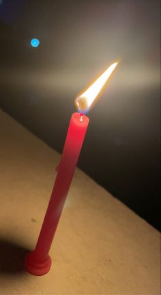 a single red candle with a bright light shining on it's side in the dark