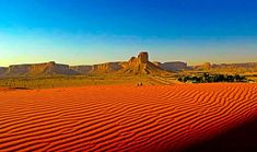 the desert is covered in red sand with mountains in the background