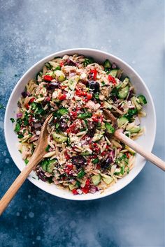 a white bowl filled with pasta salad and two wooden spoons on top of it