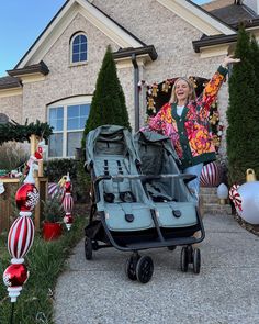 a woman standing in front of a house with her baby stroller and christmas decorations