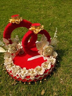 a red heart shaped box with flowers and leaves on the top sitting in the grass