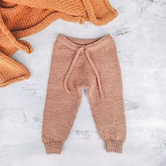 a knitted baby's pants and sweater on a white surface with an orange blanket