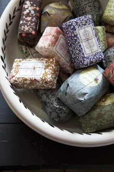 a white bowl filled with lots of different colored wrapped presents on top of a table