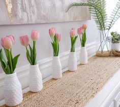 pink tulips are in white vases lined up on a burlap mat