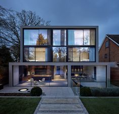 a modern house with glass walls and stairs leading up to the front door, at night